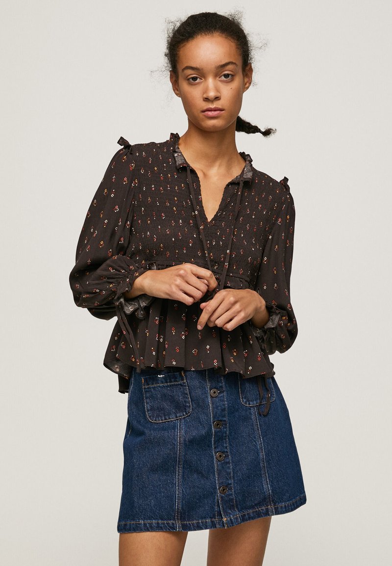 Blusa nera a fiori con maniche a sbuffo e scollatura a V profonda, abbinata a una gonna in denim blu con bottoni frontali e due tasche.