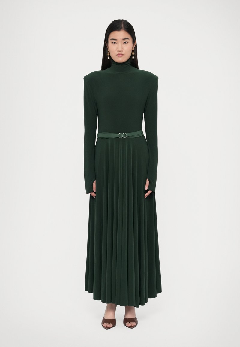 Tumši zaļa, garroku kleita ar augstu apkakli un krokotu svārku. Ir josta ar dubultu apaļu sprādzēm un teksturētu audumu.