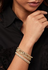 Gouden armbanden set met meerdere strengen met verschillende texturen, waaronder gladde en gefacetteerde kralen, sommige geaccentueerd met heldere kristallen.