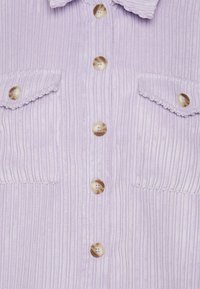 Světlofialová manšestrová košile s žebrovanou strukturou, vybavená šesti knoflíky a dvěma náprsními kapsami. Knoflíky mají kulatý, hladký design.