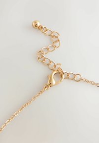 Cadena de color dorado con formas ovaladas unidas, que cuenta con un cierre de langosta y una sección ajustable con un acento de cuentas redondas.