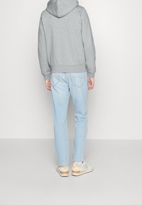Sudadera gris, jeans de mezclilla azul claro y zapatillas beige con acentos naranjas. Tejido suave, ajuste casual y detalles de costura visibles en los jeans.