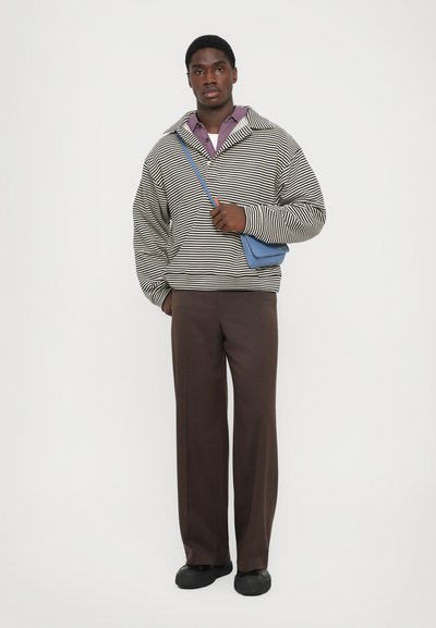 Sweatshirt rayé en noir et blanc, coupe décontractée, associé à un pantalon large marron. Les accessoires comprennent un petit sac bandoulière bleu.