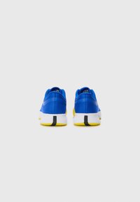 Baskets de sport bleues avec un dessus en tissu texturé, une semelle intermédiaire blanche et une semelle extérieure jaune. Présentent un col rembourré et des accents noirs stratégiques.