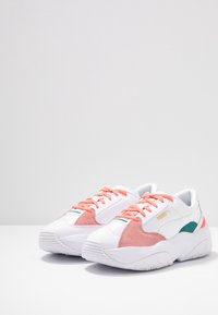 Sneaker mit einem weißen Mesh- und Synthetik-Obermaterial, pinken Wildlederelementen, grünen Details und einer dicken weißen Gummisohle. Schnürsenkel in passendem Pink.