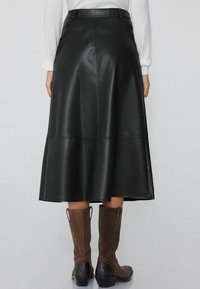 Falda midi de cuero negro con un diseño acampanado, que presenta una textura suave y costuras visibles. Combinada con botas marrones hasta la rodilla.