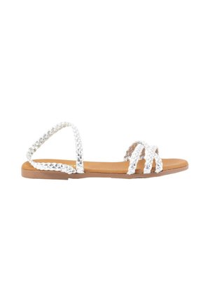 Correas trenzadas blancas con una suela plana color marrón. Diseño de punta abierta. Presenta múltiples bandas cruzando el pie para ofrecer soporte. Estilo minimalista.