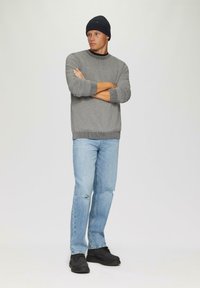 Grau gestrickter Pullover mit gerippten Bündchen und Saum, kombiniert mit hellblauen, zerrissenen Jeans und schwarzen Schnürschuhen. Ein Hut in dunkler Farbe rundet das Outfit ab.