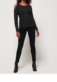 Maglione nero a spalle scoperte con motivo testurizzato, polsini a costine; abbinato a jeans skinny neri strappati e stivali alla caviglia.