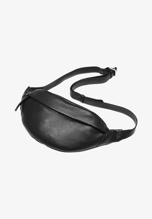 Banane en cuir noir avec sangle réglable et boucle argentée sur fond blanc, fermeture éclair partiellement recouverte par un rabat.