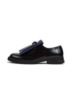 Mocassin en cuir noir avec semelle plate, bride bleu marine et détail nœud noir, vue de côté sur fond blanc.