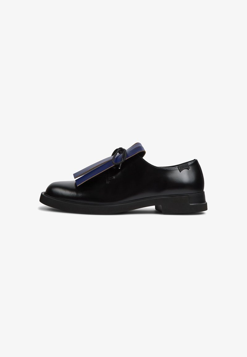 Mocassin en cuir noir avec semelle plate, bride bleu marine et détail nœud noir, vue de côté sur fond blanc.