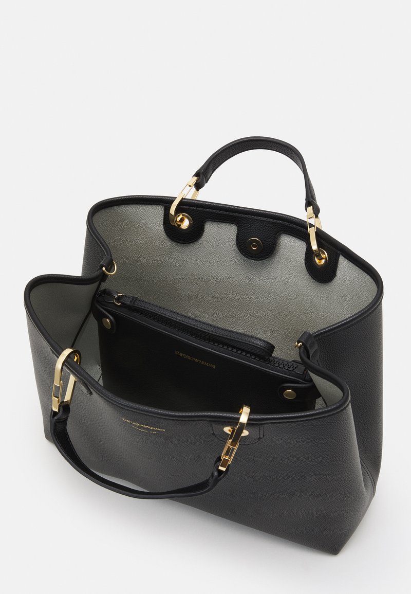 Borsa tote in pelle nera con hardware dorato, dotata di un ampio interno e una tasca con zip, foderata in tessuto grigio chiaro.