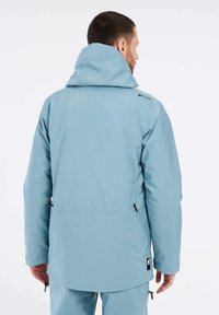 Lichtblauwe, waterdichte jas met capuchon. Voorzien van verstelbare manchetten en zijritsen. Gladde textuur, eenvoudig ontwerp en logo op de schouder.