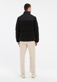 Sort pufferjakke med tekstureret fleece materiale og en glat sort overdel. Bæres med beige cargo bukser og hvide sneakers.