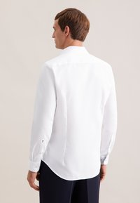 Camicia bianca a maniche lunghe con taglio sartoriale, colletto a punte e polsini con bottoni, caratterizzata da una texture liscia e orlo arrotondato.