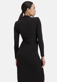 Schwarzes langärmliges Kleid mit einer taillierten Silhouette, das ein Wickeldesign und einen seitlichen Schlitz aufweist. Aus weichem, dehnbarem Stoff und glatter Textur.