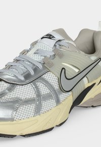 Nærbillede af en grå og beige Nike sneaker med hvide snørebånd, mesh overdel, gummisål og sort Nike swoosh-logo på siden.