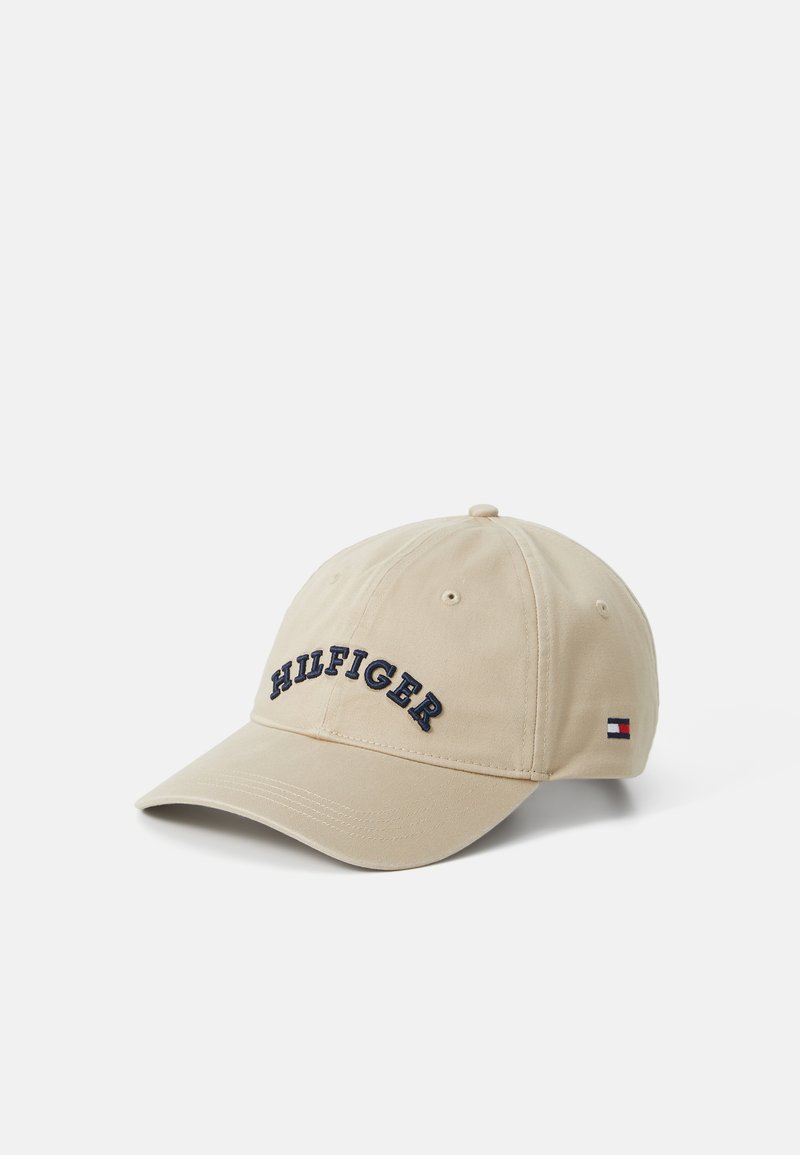 Beige baseballcaps laget av bomull med brodert "HILFIGER"-tekst i marineblått. Har en buet skygge og et lite logomerke på siden.