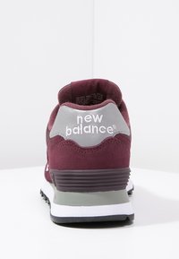 Sneaker in suede color bordeaux con accenti grigi, collo imbottito e testo del logo bianco. Presenta una suola testurizzata e elementi di design stratificati.