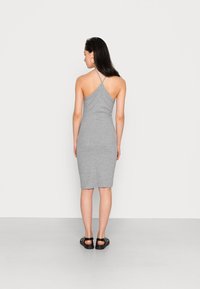 Vestido cinza sem mangas com uma silhueta justa, alças cruzadas nas costas e bainha até o joelho. Usado com sandálias pretas sobre um fundo plain.