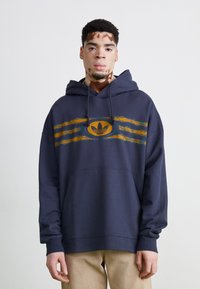 Mørkeblå hettegenser med gule og oransje grafiske striper og et sentralt logo, med en frontlomme og ribbede mansjetter.
