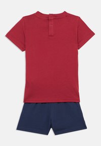 Κόκκινο βαμβακερό T-shirt με κοντά μανίκια και κλείσιμο με κουμπί στο πίσω μέρος, συνδυασμένο με ναυτικό μπλε βαμβακερές βερμούδες σε απλό, χαλαρό σχήμα.