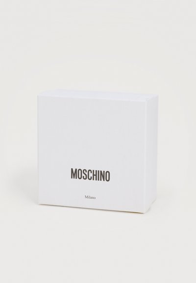 Λευκό ορθογώνιο κουτί συσκευασίας Moschino Milano με μαύρο κείμενο σε απλό ανοιχτό φόντο, όρθιο και ελαφρώς γωνιασμένο.