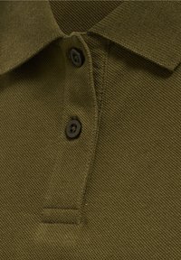 Gros plan sur le col d’un polo vert olive texturé avec deux boutons foncés partiellement attachés sur la patte de boutonnage.