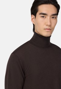 Temno rjav, rebrast pulover s turtleneck izrezom in prilegajočim dizajnom. Ima visok ovratnik in mehak material, primeren za nošenje v plasteh ali samostojno.