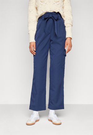 Navy wide-leg trousers with a tied waist, side pockets, and a soft texture, paired with white athletic shoes and light socks.