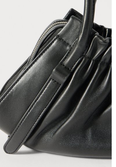 Μαύρη δερμάτινη τσάντα με ελαστικά στοιχεία, ραμμένη λαβή και ορατό ασημένιο φερμουάρ κατά μήκος της άνω πλευράς.