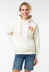Crème hoodie met koorden, met een kleurrijke graphic op de borst. Gecombineerd met denim shorts. Zacht materiaal en een relaxte pasvorm.