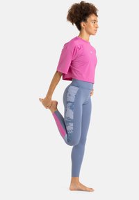 Camiseta deportiva rosa cortada combinada con leggings azules que presentan acentos de patrón floral a lo largo de los costados. Los materiales lucen suaves y elásticos.
