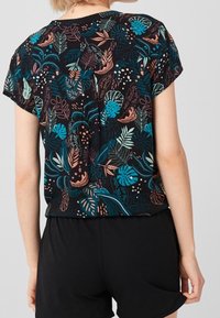 Top nero con motivi di foglie colorate in teal, corallo e bianco, dal taglio morbido e maniche corte, abbinato a pantaloni corti neri.