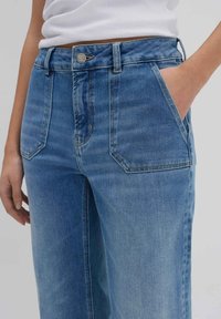 Jeans in denim azzurro chiaro con un taglio comodo, dotati di tasche anteriori, chiusura con bottone e leggera scoloritura. Il tessuto ha una texture liscia.