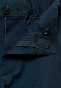 Navy blue fabric with a zipper and button closure, featuring a textured waistband and horizontal stitching near the pocket area.
