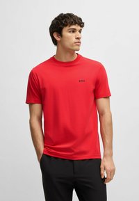 Rød bomulds T-shirt med rund hals og korte ærmer. Har et lille sort logo på den øverste venstre bryst. Glat tekstur og tætsiddende design.