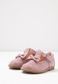 Różowe buty z lakierowanej skóry z perforowanymi detalami, okrągłym czubkiem i ozdobną kokardką. Posiadają rzep do łatwego zapinania.