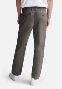Pantaloni in tela grigi da uomo con gamba dritta, dotati di due tasche posteriori e vita piatta, abbinati a sneakers bianche.