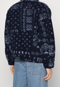 Giacca in fleece blu navy con texture a motivo, caratterizzata da design azzurri. Include un colletto e bottoni a pressione, con una vestibilità comoda.
