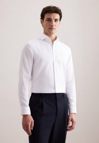 Witte blouse met lange mouwen, een getailleerd ontwerp, een gladde textuur en een knoopsluiting aan de voorkant, gecombineerd met donkerblauwe, op maat gemaakte broek.