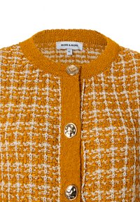 Gevoerde oranje cardigan met wit geweven patroon, voorzien van een ronde kraag en drie gouden knopen aan de voorkant, label zichtbaar aan de binnenkant.