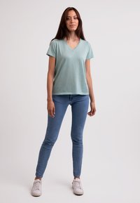 Mincově zelené tričko s výstřihem do V a krátkým rukávem, kombinované se světle modrými úzkými džíny a bílými teniskami; hladký materiál, volný střih a minimalistic design.