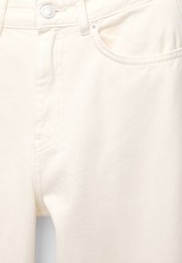 Jean en denim beige clair avec une coupe droite, présentant une poche avant, un système de fermeture à bouton et une texture subtile dans le tissu.