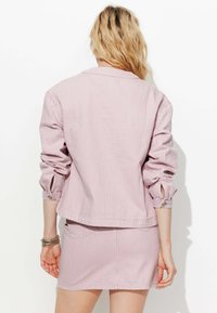 Veste rose rayée à manches mi-longues et poignets boutonnés, associée à une jupe mini assortie, présentée de dos.