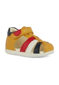 Sandalia de cuero amarilla con franjas rojas, blancas y marinas. Cuenta con una correa de velcro y un diseño abierto para mayor transpirabilidad. Suela suave blanca.