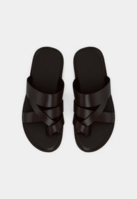 Black slide sandals made of smooth synthetic material, featuring crisscross straps and a flat sole. Minimalist design with a matte finish.