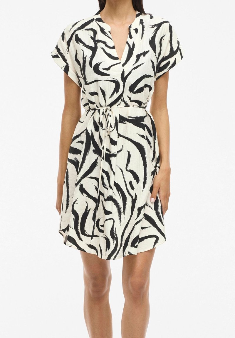 Vestido de manga corta con escote en V, con un patrón abstracto en blanco y negro, detalle de cintura con lazo y tejido ligero texturizado.