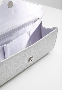 Srebrna torebka wieczorowa z brokatem i satynowym wnętrzem, z zapięciem na zatrzask oraz wieloma przegródkami do organizacji. Gładka tekstura i wyraźnie zarysowany kształt.